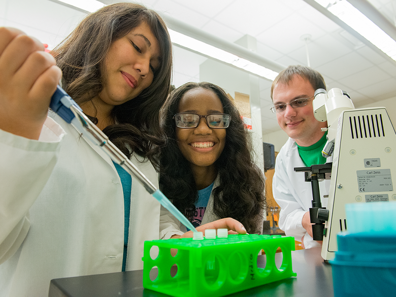 Undergraduate researchers use a micropipette in their microbiology studies.
